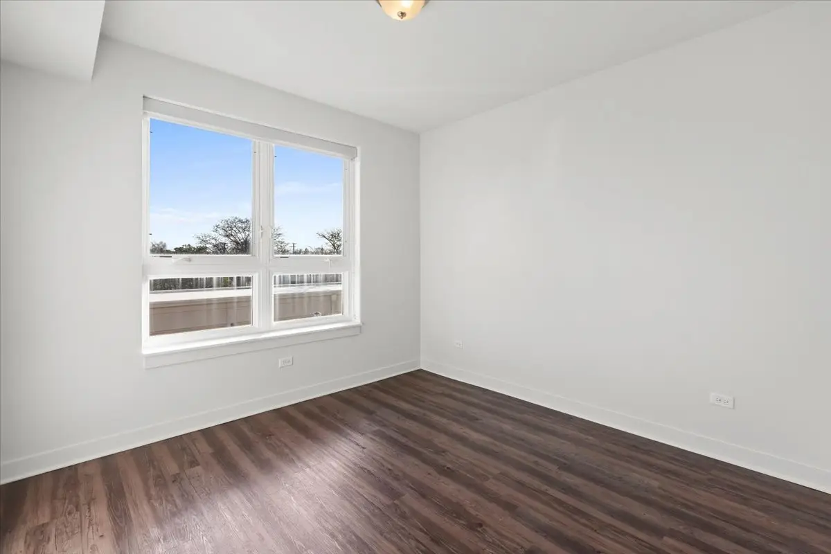 bedroom with large window, white walls with tall baseboards, and dark brown wood style flooring.