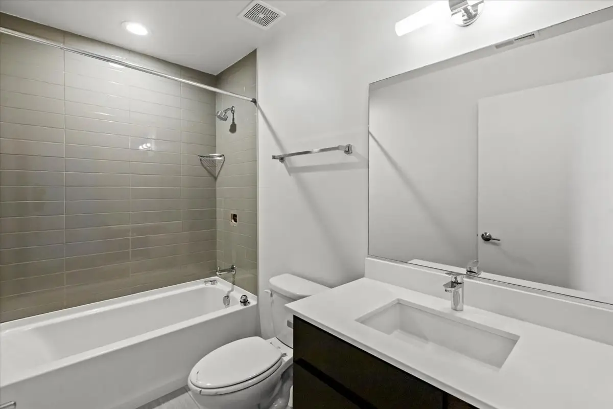 bathroom with modern vanity, custom light fixture, and shower bath combo with gray subway tile.
