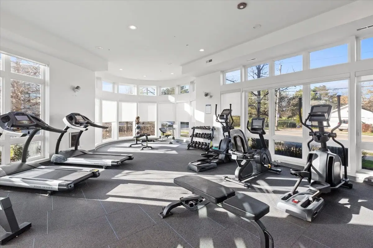 Fitness center with windows from the floor to ceiling, electric shades, padded flooring, free weights, elipticals, rowing machine, seated bike, and treadmills.